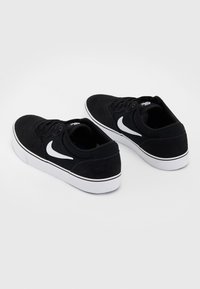 Czarne zamszowe sneakersy z białym logo Nike, sznurowane, w klasycznym niskim kroju, z białą gumową podeszwą i czarnymi akcentami.