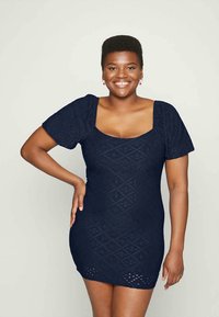 Vestido curto azul-marinho com mangas bufantes, tecido texturizado com padrões de diamantes e decote quadrado. Silhueta justo ao corpo.