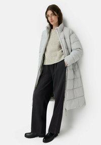 Lys grå lang pufjakke med høj krave, ribbet beige sweater, sorte vidde bukser og sorte ankelstøvler. Glat tekstur, polstret design.