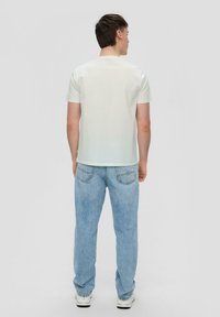 Lichtgekleurde, kortekorte t-shirt met een ronde halslijn, gecombineerd met vervaagde blauwe jeans en witte sneakers, gezien vanuit de achterkant.