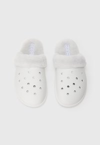 Ett par vita slip-on träskor med ventilationshål och mjukt fleecefoder på en enkel vit bakgrund.