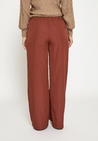 Wijde broek in roestkleur, met een elastische tailleband en een lichtgewicht, gekreukte stof. Minimalistisch ontwerp zonder patronen.