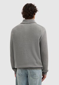 Grijze geribbelde trui met een brede kraag, voorzien van lange mouwen en een relaxte pasvorm. De achterkant heeft een gladde textuur en minimale naden.