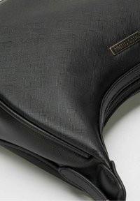 Bolso de mano negro con textura, bordes estructurados, cremallera visible y una pequeña etiqueta de metal rectangular de la marca en la esquina superior.