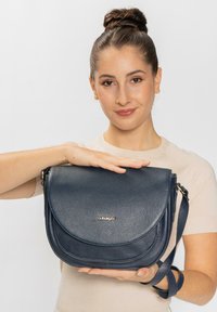 Bolso de cuero cruzado de color marino con un acabado texturizado, cierre de solapa redondeado y correa ajustable, que presenta un acento de logo en la parte frontal.