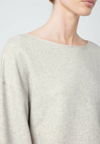 Pull en laine gris clair à la coupe oversize, avec un col large et une texture douce, doté d'épaules tombantes et d'une coupe décontractée. Aucun motif ni accent visible.