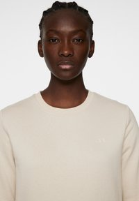 Beige sweatshirt met een ronde halslijn, ribgebreide manchetten en een subtiele logo op de borst. Zachte stof met een gladde textuur.