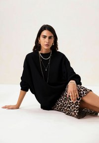 Sweatshirt oversize noir à manches longues, associé à une jupe léopard. Les accessoires comprennent des colliers superposés et des bagues.