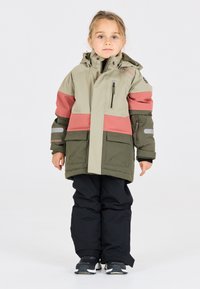 Chaqueta de exterior para niño en verde claro y coral, con bolsillos grandes, capucha ajustable y detalles reflectantes; combinada con pantalones de nieve negros.
