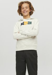 Felpa grigia chiara con tasca a marsupio, dotata di una patch con logo multicolore. Abbinata a pantaloni neri, che presentano un design casual.