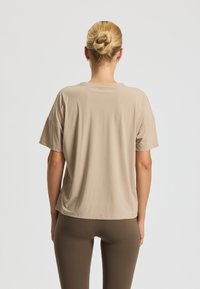 Beige, loose-fitting t-shirt with short sleeves, round neck, and smooth texture, paired with dark brown leggings. Simple, modern design.