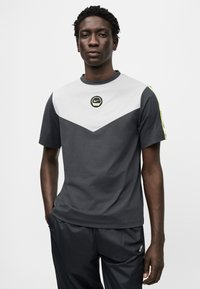 Μπλούζα Nike με σχεδιασμό με γκρι και ανοιχτό γκρι μπλοκ χρωμάτων. Μανίκια κοντά, στρογγυλή λαιμόκοψη και εξαγωνικό λογότυπο στο κέντρο.