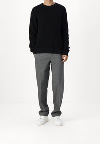 Maglione nero a maglia con texture a coste, abbinato a pantaloni grigi e sneakers bianche. L'outfit presenta una vestibilità comoda e un design semplice.