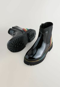 Botas de tobillo impermeables negras con un acabado brillante, que cuentan con un panel de elastano acanalado, un acento de rayas de arcoíris y una suela de goma texturizada.