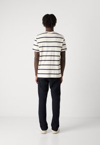 Kortærmet stribet skjorte i creme med marineblå striber, sammen med mørke bukser. Minimalistisk design, blød tekstur og afslappet pasform.