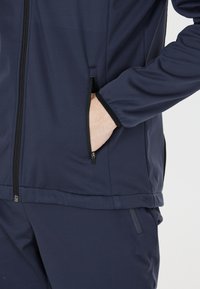 Marinefarbener Sportjacke mit glatter Textur, durchgehendem Reißverschluss, Seitentaschen und kontrastierenden schwarzen Akzenten entlang des Reißverschlusses und der Manschetten.