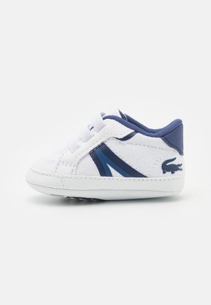 Weiße Sneakers mit marineblauen Akzenten, strukturiertem Stoff, Schnürverschluss und einer Gummisohle mit einem Logodetail an der Ferse.