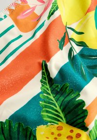 Színes textília élénk narancssárga, türkiz és krém csíkokkal, trópusi levelek és gyümölcsök mintázatával, sima textúrával és élénk kialakítással.