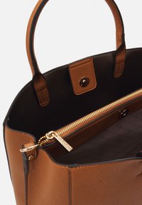 Sac à main en cuir marron avec un extérieur texturé, fermeture éclair dorée et intérieur noir. Il dispose de deux poignées et d'une fermeture à pression en haut.