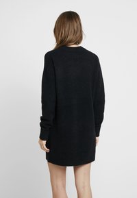 Abito maglione nero a maglia con maniche lunghe, scollatura rotonda e vestibilità leggermente oversize. Texture morbida, lunghezza a metà coscia, senza motivi visibili.