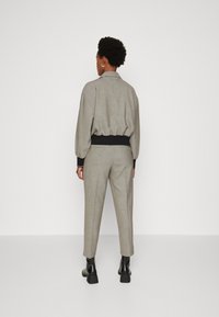 Grau karierte Bomberjacke mit elastischem Bund, kombiniert mit passenden Hosen. Beide haben eine lockere Passform und schwarze Akzente an den Bündchen und am Taillenbund.