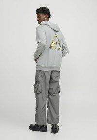 Grå hoodie med en gul och svart triangeldiagram på baksidan, tillsammans med grå cargo-byxor och svarta stövlar.