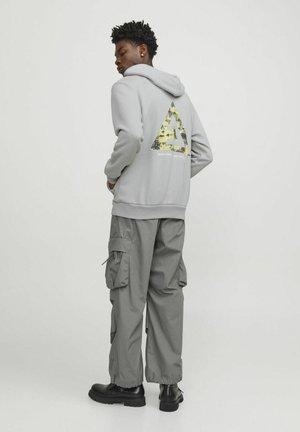 Gray hoodie with a yellow and black triangle graphic on the back, paired with gray cargo pants and black boots.