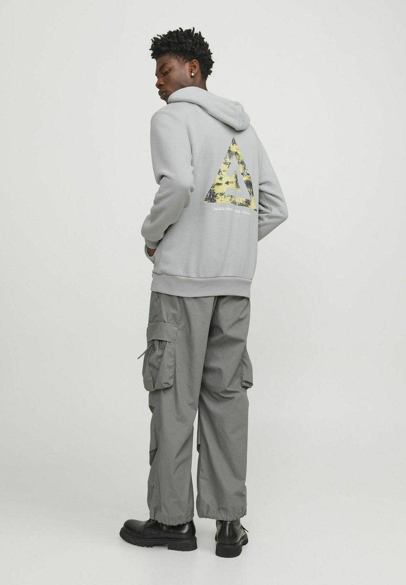 Grå hoodie med en gul och svart triangeldiagram på baksidan, tillsammans med grå cargo-byxor och svarta stövlar.