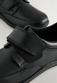 Chaussures en cuir noir avec des brides Velcro. Présentent une texture lisse, des accents cousus et une pointe arrondie. Conviennent pour un usage décontracté ou formel.