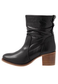 Bottine en cuir noir à design décontracté, bout pointu et talon bloc en bois. Présente des coutures décoratives sur les côtés.