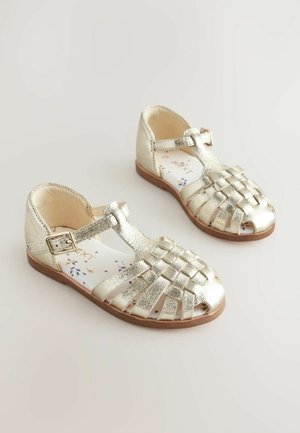 Sandales en cuir métallisé doré avec un design tissé, bout ouvert et sangle à boucle ajustable. Semelle intérieure à motifs floraux, semelle plate marron.