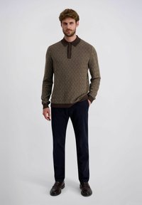Braun gemusterter Pullover mit einem dunklen Kragen und Knöpfen, kombiniert mit dunklen blauen Hosen und dunkelbraunen Schuhen. Strukturiertes Strickmaterial und enganliegendes Design.