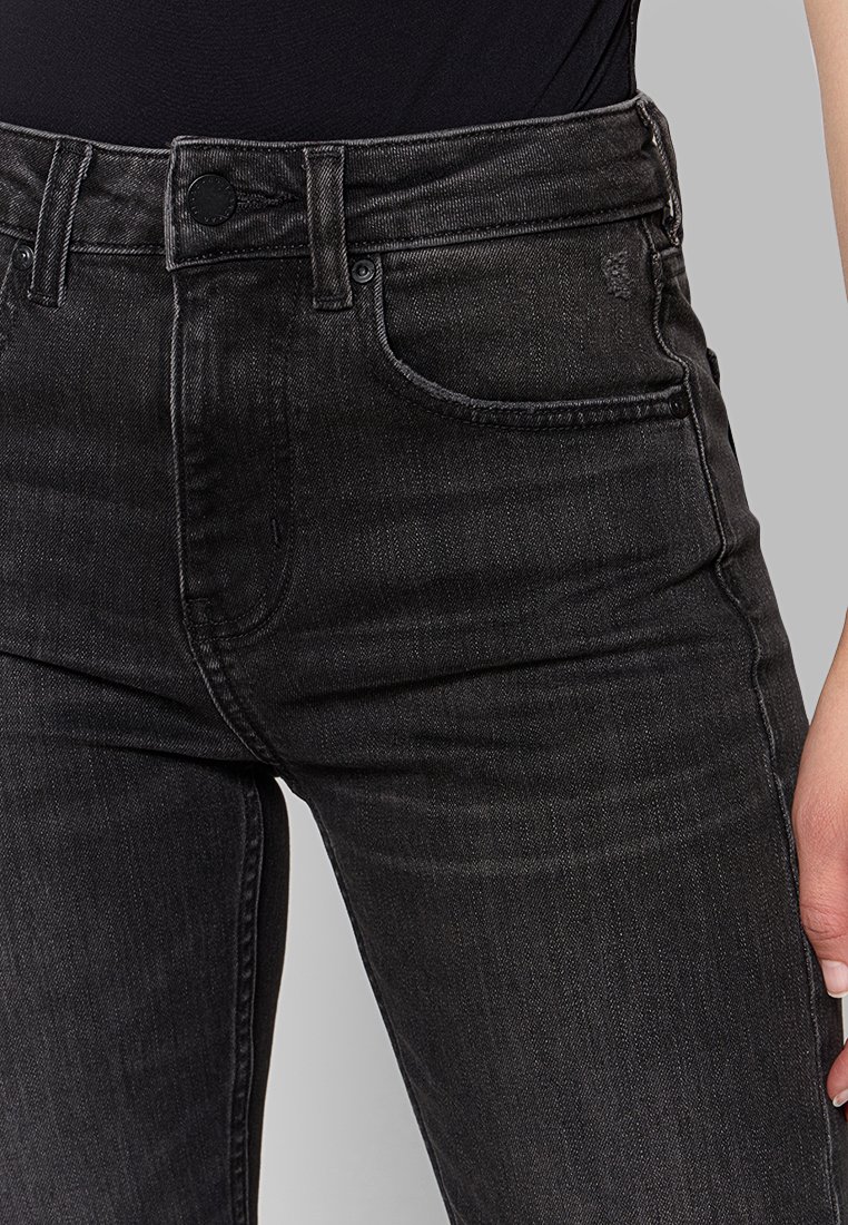 Czarne dżinsy o wysokim stanie, z pięcioma kieszeniami i subtelnymi detalami przeszycia. Tekstura jest gładka z delikatnym efektem zużycia.