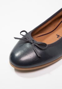 Ballerine plate en cuir noir avec bout arrondi, nœud décoratif à l'avant et semelle intérieure beige rembourrée avec logo de marque visible.