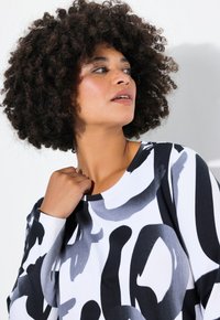 Top lungo a maniche nere e bianche con pattern astratti, dotato di scollatura rotonda, realizzato in tessuto morbido e con vestibilità rilassata.
