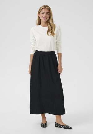 Sort maxi nederdel med elastisk talje, parret med en langærmet hvid top. Sorte flade sko med sølvnitter fuldender outfittet.