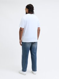 Valge puuvillane T-särk ümmarguse kaelusega, kombineeritud laia lõikega siniste teksadega ja valgete tossudega, nähtud tagantpoolt.