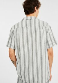 Korte mouwen shirt van lichte stof met verticale zwart-witte strepen, voorzien van een standaardkraag en een rechte achterpand.