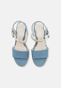 Sandales en denim bleu avec des brides beiges à la cheville et une large bande à l'avant. Elles disposent d'une semelle texturée et d'une boucle réglable pour un maintien sécurisé.