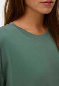 Olijf groene korte mouwen shirt met een ronde halslijn, een gladde textuur en subtiele stiksels rondom de halslijn.