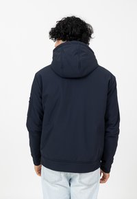 Marineblaues Kapuzenjackett mit glatter Textur, geripptem Bund und einer seitlichen Ärmeltasche. Mit einem gewölbten Kapuzendesign und genähten Nähten.