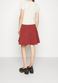 Top de punto acanalado beige claro con mangas abullonadas cortas, combinado con una falda acampanada burdeos con paneles en capas y cintura alta. Zapatos de plataforma negros.