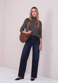 Col roulé à motifs noir et blanc, jean taille haute bleu, sac bandoulière en daim marron, ballerines noires pointues, debout sur un fond clair.