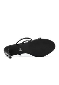 Sandales à talons hauts noires avec des fines lanières ornées d'accents en cristal. Semelle noire texturée avec un détail de logo. Design simple et apparence élégante.