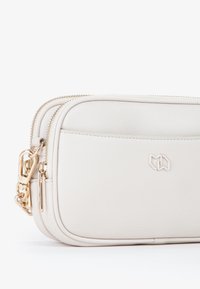 Borsa a tracolla bianca in pelle con chiusura a zip, hardware dorato e logo impresso. Texture liscia e forma rettangolare compatta.