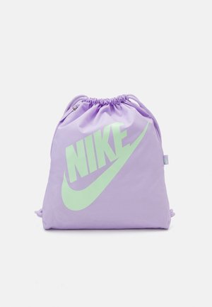 Lawendowa torba Nike z sznurkiem, z dużym bladozielonym logo Nike i znakiem Swoosh z przodu, zamknięta u góry ściąganym sznurkiem.