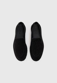 Svarte semskede slip-on sko med en glatt tekstur, rund tå og kontrasterende søm langs kantene. Minimalistisk design uten maskinvare.