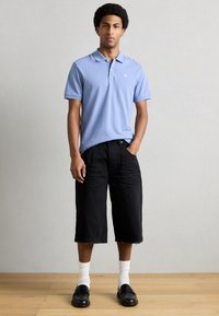 Ανοιχτό μπλε πόλο πουκάμισο, μαύρα σορτς μήκους μέχρι το γόνατο, λευκές κάλτσες και μαύρα μοκασίνια. Λείο ύφασμα, casual εφαρμογή και σχέδιο με γιακά με ρίγα.