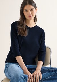 Haut bleu marine à manches longues avec un col rond, associé à un jean en denim bleu clair. Le tissu semble doux avec une texture lisse.