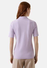 Lila Poloshirt mit klassischem Kragen und kurzen Ärmeln. Glatte Textur, taillierte Passform und subtile Nähedetails am Saum.